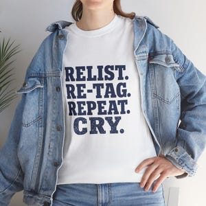May include: A white short-sleeved t-shirt featuring the dark blue distressed text RELIST. RE-TAG. REPEAT. CRY. layered under a light blue denim jacket with metal buttons and a classic collar, paired with blue denim jeans.
