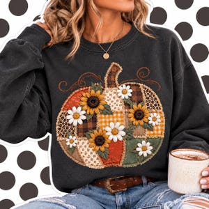 Puede incluir: Una sudadera gris carbón de manga larga con un gran gráfico central de una calabaza compuesta por varios patrones de patchwork, incluyendo estampado de leopardo, cuadros y vichy, decorada con girasoles amarillos y margaritas blancas.