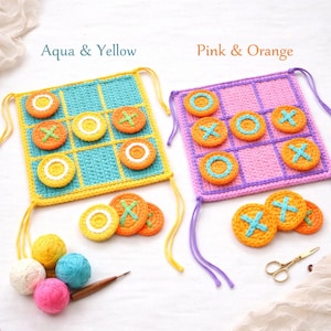May include: Crocheted tic-tac-toe game sets in aqua and yellow, and pink and orange. Each set includes a crocheted grid and game pieces. The aqua and yellow set has yellow trim and the pink and orange set has purple trim. The text "Aqua & Yellow" and "Pink & Orange" are visible.