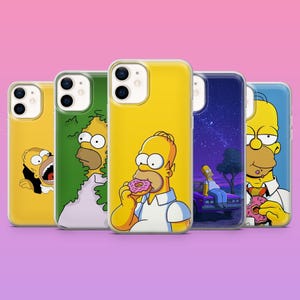 Puede incluir: Cinco fundas de teléfono con imágenes de Homer Simpson. Las fundas tienen fondos amarillos, verdes y azules. Una funda muestra a Homer comiendo una rosquilla rosa. Están alineadas sobre un fondo rosa y morado.