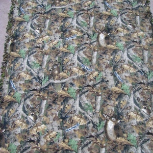 May include: A camouflage fleece blanket with a repeating pattern of deer and the words "RealTree" throughout. The blanket has a fringed edge.