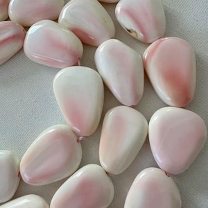 May include: A collection of smooth, polished, irregular pebble-shaped beads in shades of creamy white and soft pastel pink. Each bead features a glossy, rounded surface and is strung together, showcasing natural color variations and organic shapes.