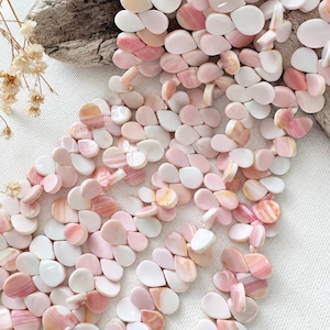May include: A collection of teardrop-shaped beads in various shades of soft pink, cream, and white. The beads feature smooth, polished surfaces with subtle natural color variations and striations, arranged in a loose, overlapping cluster.