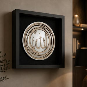May include: A square black shadow box frame containing a circular mirror. Centered on the mirror is a light brown, laser-cut wooden Arabic calligraphy script of the word Allah, surrounded by an intricate, swirling circular wooden border design.