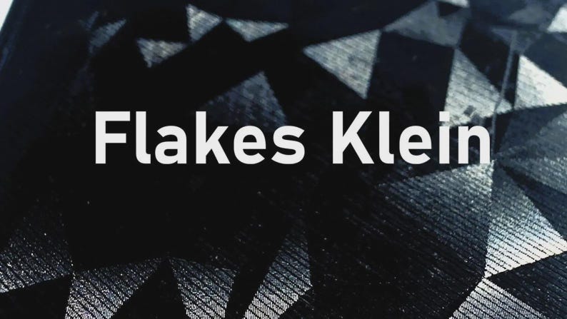K&ouml;nnte beinhalten: Abstrakter Hintergrund mit einem geometrischen Muster in Schwarz- und Graut&ouml;nen. Der Text "Flakes Klein" ist wei&szlig; dargestellt und mittig im Bild platziert. Das Design hat eine moderne und minimalistische &Auml;sthetik.
