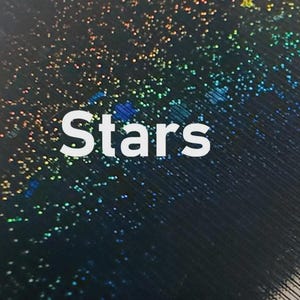 K&ouml;nnte beinhalten: Abstraktes Bild mit dem Wort "Stars" in Wei&szlig;. Der Hintergrund ist dunkel und mit kleinen, bunten, irisierenden Punkten bedeckt, die an einen Sternenhimmel erinnern. Das Design hat eine schimmernde, himmlische Qualit&auml;t.