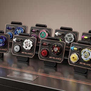 May include: A collection of eight Beyblade X spinning tops displayed on individual black stands with copper-colored trim. Each stand features the Beyblade X logo and holds a spinning top along with a small launcher component in various colors.