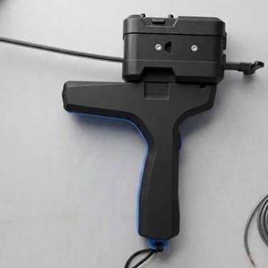 Könnte beinhalten: Ein schwarzes Handwerkzeug mit Pistolengriff und einem blauen Akzent am Abzugsbereich. Das Gerät verfügt über einen rechteckigen oberen Teil mit zwei sichtbaren silbernen Schrauben und einem langen, dünnen schwarzen Stab, der seitlich absteht.