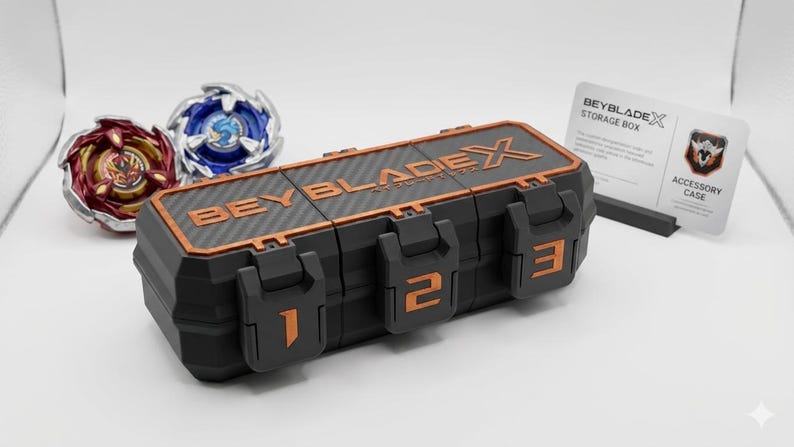 K&ouml;nnte beinhalten: Schwarze und orangefarbene Beyblade X Aufbewahrungsbox mit drei nummerierten F&auml;chern. Zwei Beyblades, eines rot und gold, das andere blau und silber, sind sichtbar. Eine Zubeh&ouml;rkartenkarte ist ebenfalls vorhanden.
