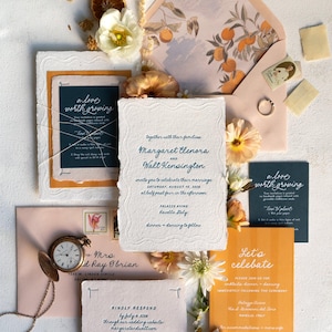 May include: Wedding invitation suite with floral and citrus accents. Includes invitation cards, envelopes, and a pocket watch. The invitation text reads "Margaret Elenora and Walt Kensington invite you to celebrate their marriage."