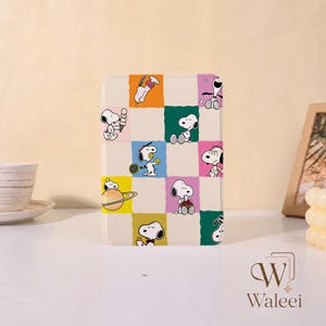 Peut inclure: Une coque de tablette rectangulaire avec un motif en damier composé de carrés colorés orange, verts, bleus, roses, jaunes et blancs. Chaque carré présente une illustration du personnage Snoopy effectuant diverses activités comme jouer au tennis, manger une glace ou s'asseoir sur une planète.