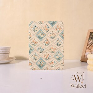 May include: A rectangular tablet case featuring a repeating diamond pattern filled with small blue, orange, and white floral illustrations on a cream background. The design is symmetrical, with each diamond containing a distinct bouquet of flowers.