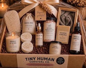 May include: A gift basket containing a candle labeled Mentally at the Spa, a pouch of shower steamers, a bottle of body oil, bath soak, a bar of soap, a spray bottle labeled Tired as a Mother, and a scrub, all with Tiny Human Survival Co. branding.