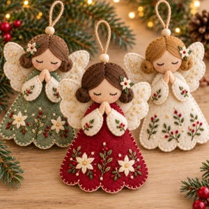 May include: Three felt angel ornaments with embroidered details. Each angel has closed eyes, hands in prayer, and wings. The dresses are green, red, and cream, featuring floral embroidery with white flowers and red berries. Each has a jute hanging loop.