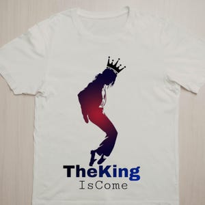 May include: White t-shirt featuring a silhouette of a person wearing a crown, in a dance pose. The silhouette is shaded in red and blue. The text "The King Is Come" is printed below the silhouette in black and blue.