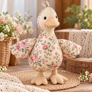 May include: A plush duck toy featuring a cream-coloured fabric body adorned with a pink and green floral pattern. The duck has a solid tan beak, matching tan webbed feet, and small black eyes. A small tuft of fabric sits atop its head.