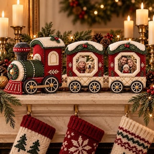 Op de afbeelding: Een vilten kersttreindecoratie met een rood-groene locomotief en twee wagons met achthoekige fotolijstjes. De trein is versierd met wit stiksel, goudkleurige wielen en kleine groene hulstaccenten op de daken van de wagons.