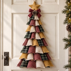 May include: A wall-hanging Christmas tree decoration made of layered fabric scraps in mustard yellow, deep red, and dark green plaid. The tree is topped with a fabric star and a dark red bow with small pinecones, featuring frayed edges.