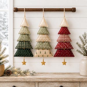 Puede incluir: Tres adornos navideños de tela en forma de árbol colgados de una barra de madera. Cada árbol consta de cinco segmentos triangulares apilados con patrones verdes, beige y rojos, con pequeñas cuentas doradas y una estrella dorada en la base.