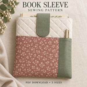 May include: A quilted book sleeve featuring a cream-colored upper section, a dusty rose floral print lower section, and a sage green fabric closure tab and side pocket. A pen is tucked into the side pocket. Text reads BOOK SLEEVE SEWING PATTERN.