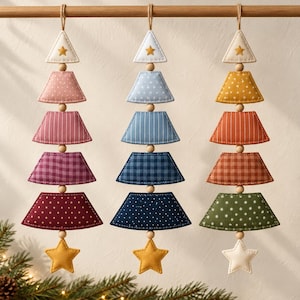 May include: Three hanging ornaments shaped like stylised Christmas trees, each composed of four stacked fabric trapezoids in varying shades of pink, blue, and earth tones, separated by wooden beads, topped with a triangle and a bottom star.