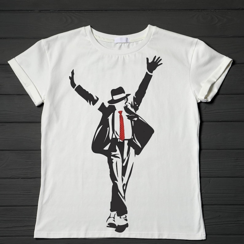 May include: White t-shirt featuring a black silhouette of a person in a hat, suit, and red tie, with arms raised. The design is a stylized illustration, likely a tribute to a famous performer. The shirt is made of a soft material.