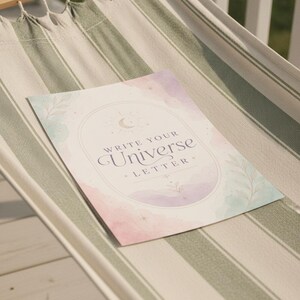 May include: A rectangular paper print featuring a pastel watercolour background in shades of pink, purple, and blue. The centre displays an arched frame with a crescent moon and star icon, containing the text "WRITE YOUR UNIVERSE LETTER".