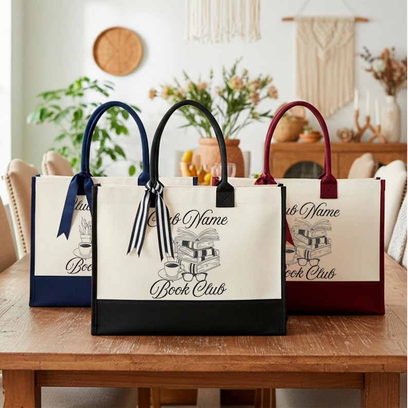 Three tote bags with the text "Book Club" printed on them, placed on a wooden table.