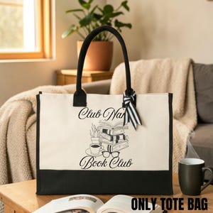 A large tote bag with the text "Club Nana Book Club" printed on it, sitting on a wooden table in a cozy living room setting.