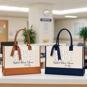 May include: Two rectangular tote bags, one with brown accents and one with navy blue accents. Both feature cream-colored panels, a floral-patterned RBT monogram, and the text Registered Behavior Technician Emily printed in black script and font.