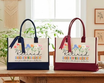 Puede incluir: Dos bolsos tote rectangulares de lona color hueso con bases de colores y lazos a juego. Los bolsos presentan un gráfico floral, el texto "Retired UNDER NEW MANAGEMENT" y "see grandkids for details" en letras negras y de colores.