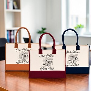 Three tote bags with the text "Book Club" printed on them, placed on a wooden surface.