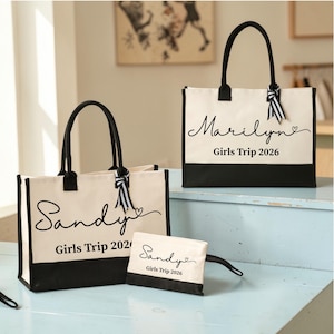 May include: Two rectangular canvas tote bags and one matching zippered pouch, all featuring a cream-colored body with a black base and black handles. Each item is personalized with black script text reading Sandy or Marilyn and Girls Trip 2026.