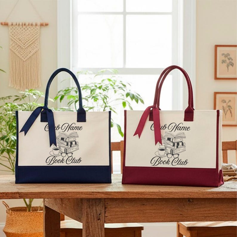 Two tote bags with the text "Book Club" printed on them, placed on a wooden table in a room with a window and plants.