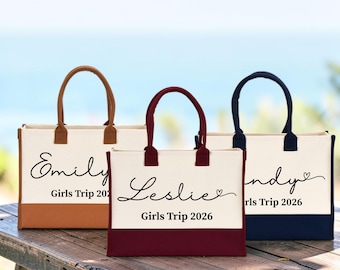 Puede incluir: Tres bolsos tote rectangulares de lona con dos asas cada uno. El bolso izquierdo tiene detalles en color canela y el nombre Emily, el central tiene detalles en granate y el nombre Leslie, y el derecho tiene detalles en azul marino y el nombre Wendy. Todos llevan el texto Girls Trip 2026.