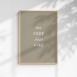 以下が含まれることがあります： 「No CODE Just VIBE」の文字が白で書かれた、くすんだ緑色の背景の額入りプリント。フレームは明るい木の色で、プリントは白い壁に掛けられています。植物の影が壁に映っています。