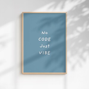 Peut inclure: Affiche encadrée avec un cadre en bois clair. L'affiche présente un fond bleu avec le texte blanc "No CODE Just VIBE" en police sans-serif. L'affiche est affichée contre un mur blanc avec des ombres.