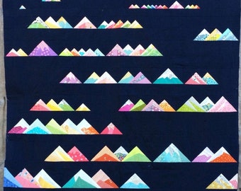 May include: A quilt with a dark blue background and rows of colorful mountain-shaped patches. The mountains are made of different fabrics and colors, creating a vibrant and playful design.