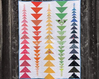 May include: A scrappy quilt with a chevron pattern in a rainbow of colors. The quilt is made up of small triangles and is finished with a blue binding. The quilt is labeled "Scrappy Small Throw Version".