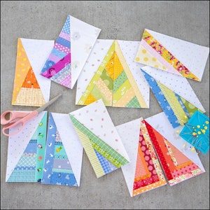 May include: Nine colorful fabric triangles with a white background. Each triangle is made of strips of fabric in different colors and patterns. The triangles are arranged in a staggered pattern on a gray surface.