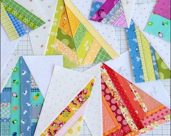Puede incluir: Una colección de nueve bloques de colcha de retazos sin terminar en varios colores y patrones, incluyendo rojo, naranja, amarillo, verde, azul y morado. Cada bloque es de forma triangular con un fondo blanco y una línea diagonal de tiras de tela.