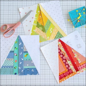 May include: Three unfinished quilt blocks in the shape of a triangle. The blocks are made of strips of fabric in various colors and patterns. The blocks are on a white gridded surface.