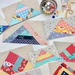 Può includere: Una collezione di triangoli di stoffa colorati, ognuno con un motivo diverso, disposti su una superficie bianca. I triangoli sono realizzati con diversi tessuti, tra cui stampe floreali, pois e motivi geometrici. I triangoli sono disposti a scalare, creando un design visivamente accattivante.