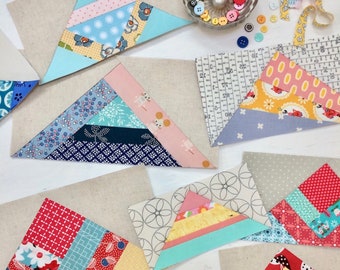 May include: A collection of colorful fabric triangles, each with a different pattern, arranged on a white surface. The triangles are made of various fabrics, including floral prints, polka dots, and geometric patterns. The triangles are arranged in a staggered pattern, creating a visually appealing design.