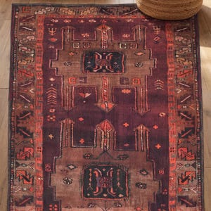 May include: A rectangular area rug featuring a deep plum and dark brown base with intricate geometric patterns in shades of orange, red, and cream. The design includes a central medallion motif, symmetrical shapes, and a detailed border pattern.