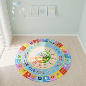 May include: A round educational area rug featuring a colorful design with the alphabet, numbers one through twelve, months of the year, and illustrations of various objects, animals, and fruits arranged in concentric circles on a light background.