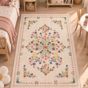 May include: A rectangular area rug with a cream background featuring a symmetrical floral pattern in shades of pink, blue, green, and yellow. The design includes small illustrations of Winnie the Pooh characters integrated into the botanical motifs.