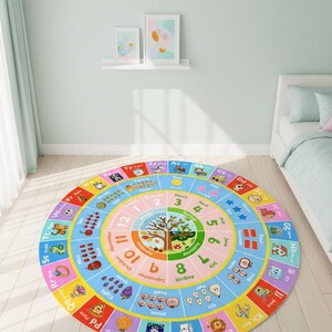 May include: A round educational area rug featuring a colorful alphabet border, a central seasonal tree illustration, and concentric rings displaying months, numbers, and counting objects with corresponding text labels in a bright, multi-colored design.