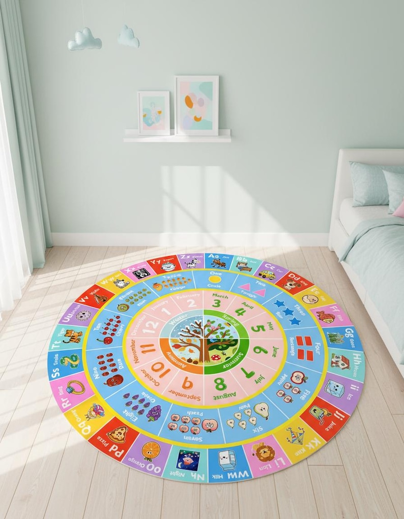 May include: A round educational area rug featuring a colorful alphabet border, a central seasonal tree illustration, and concentric rings displaying months, numbers, and counting objects with corresponding text labels in a bright, multi-colored design.