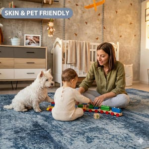May include: A large rectangular area rug featuring a distressed, mottled pattern in shades of deep blue and white. The rug has a soft, textured surface and is positioned on a floor, providing a base for a child and a small white dog playing.